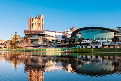 Modern waterfront cityscape with curved convention center and tall buildings reflected in calm river under clear blue sky adelaide